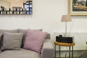 A modern living room with a grey sofa, a small wooden side table, a lamp, and a framed painting on the wall. - Refined apartment in Islington (London)