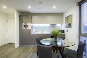 A modern kitchen with a glass dining table, grey chairs, and a potted plant.