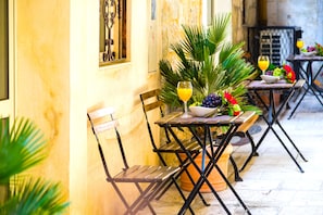Un área de comedor al aire libre con mesas y sillas de madera, una planta en maceta y un vaso de jugo de naranja.