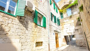 A narrow stone street with buildings featuring green shutters and a visible door. - Gaius Aurelius Valerius (Split)