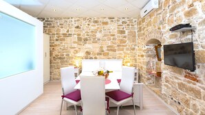 A dining area with a stone wall, a white table with chairs, and a mounted TV. - Gaius Aurelius Valerius (Split)