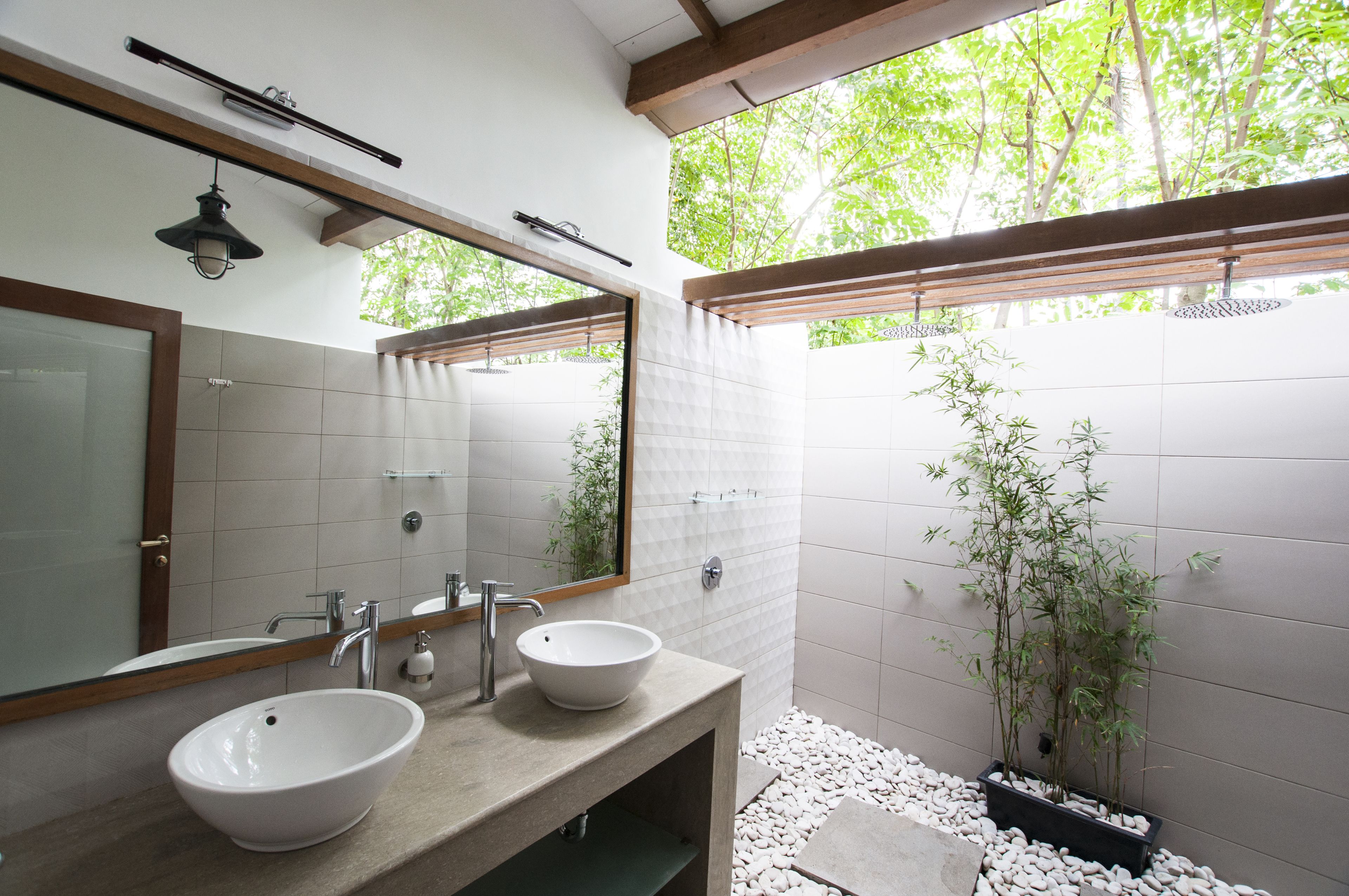 A modern bathroom with two sinks, a large mirror, and a window with a view of trees.