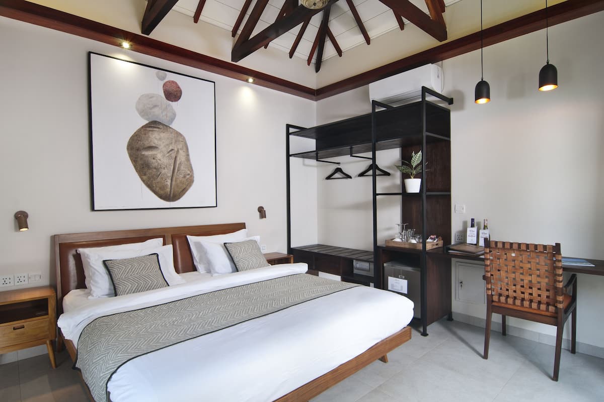 A bedroom with a bed, bedside tables, a desk, a chair, a hanging plant, and a wall-mounted shelf.