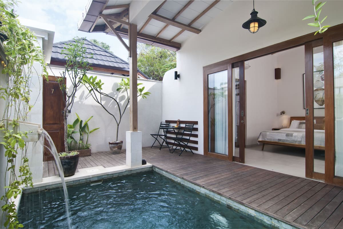 A pool area with a wooden deck, a bed, and a seating area with a bench and table.