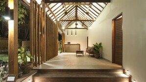 Una escalera de madera conduce a un área de recepción con un mostrador y sillas, rodeada de plantas en macetas.