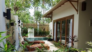 Un área de piscina con tumbonas de madera, una cerca de bambú y plantas en macetas.