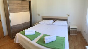 Ein ordentlich bezogenes Bett mit weißen Leinen und zwei grünen Handtüchern, ein Holzschrank, ein Nachttisch mit Lampe und ein kleiner Beistelltisch.