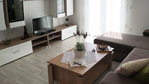 Ein modernes Wohnzimmer mit Couch, Fernseher, Bücherregal und einem Holztisch.