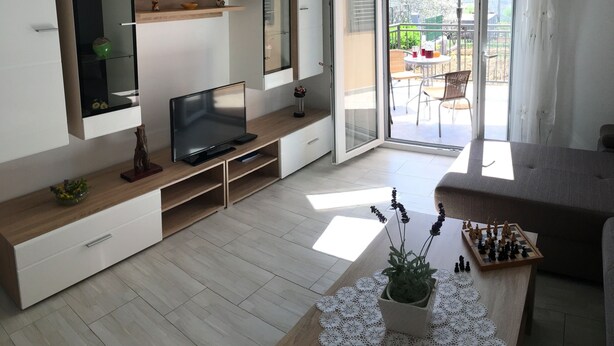 Ein modernes Wohnzimmer mit einem Flachbildfernseher, einem Couchtisch mit einem Schachspiel und einem Balkon mit Tisch und Stühlen.