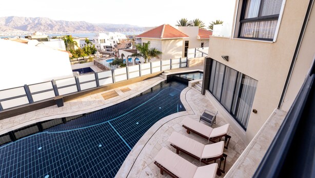 A rooftop pool area with lounge chairs, a swimming pool, and a view of the surrounding buildings and mountains. - Villa Daniela (Eilat)