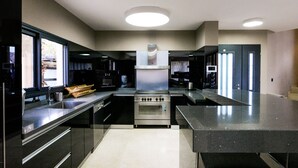 A modern kitchen with stainless steel appliances, a central island, and a large window providing natural light. - Villa Daniela (Eilat)