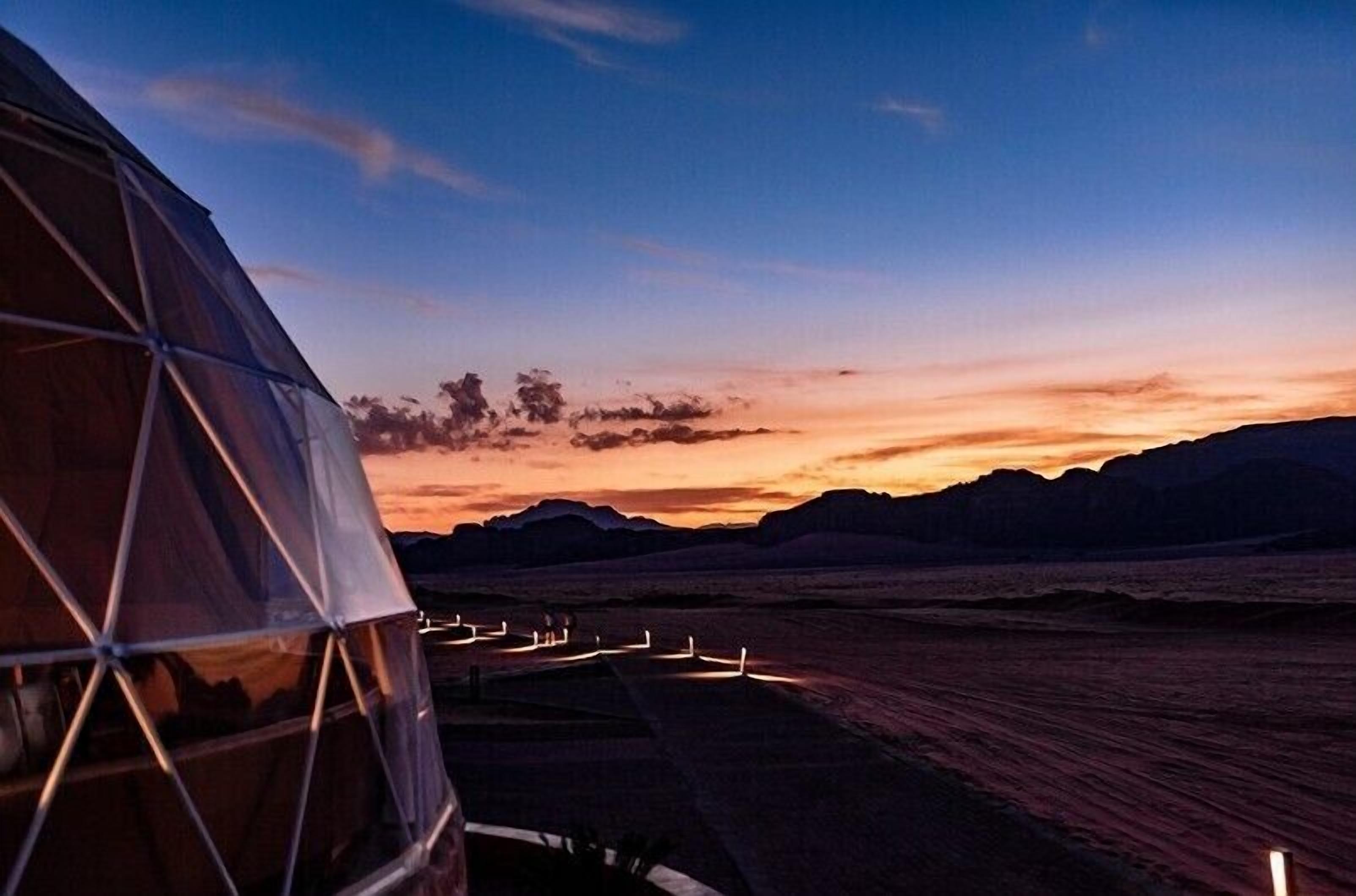 A geodesic dome structure with a view of a sunset over a desert landscape.