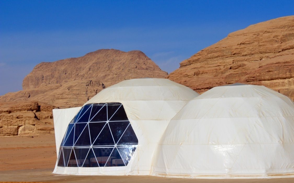 A white dome-shaped structure with a geometric window design, set against a desert landscape with rocky hills.