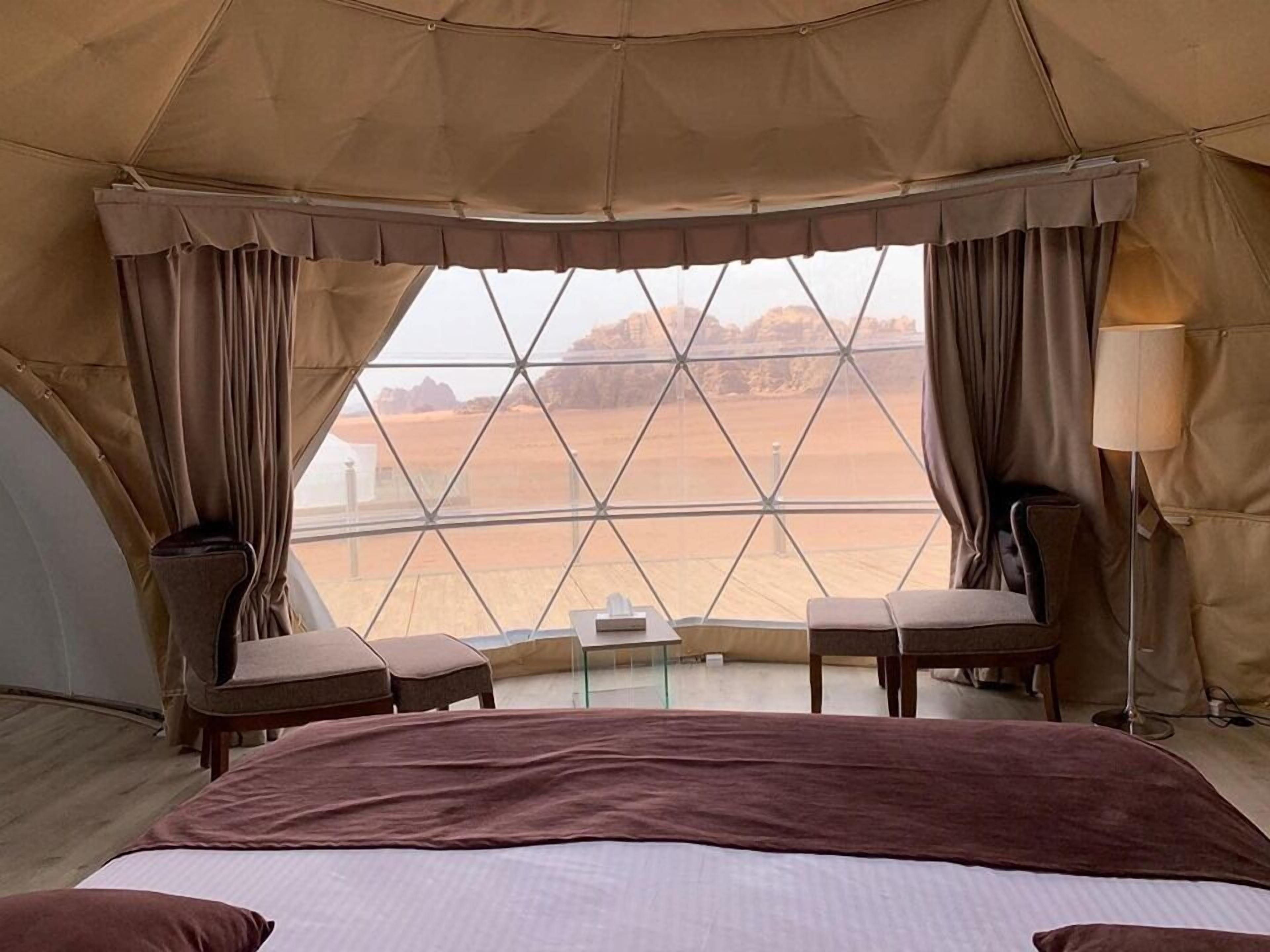 Ein Zeltraum mit einem Bett, zwei Stühlen, einem Tisch und einer Lampe.