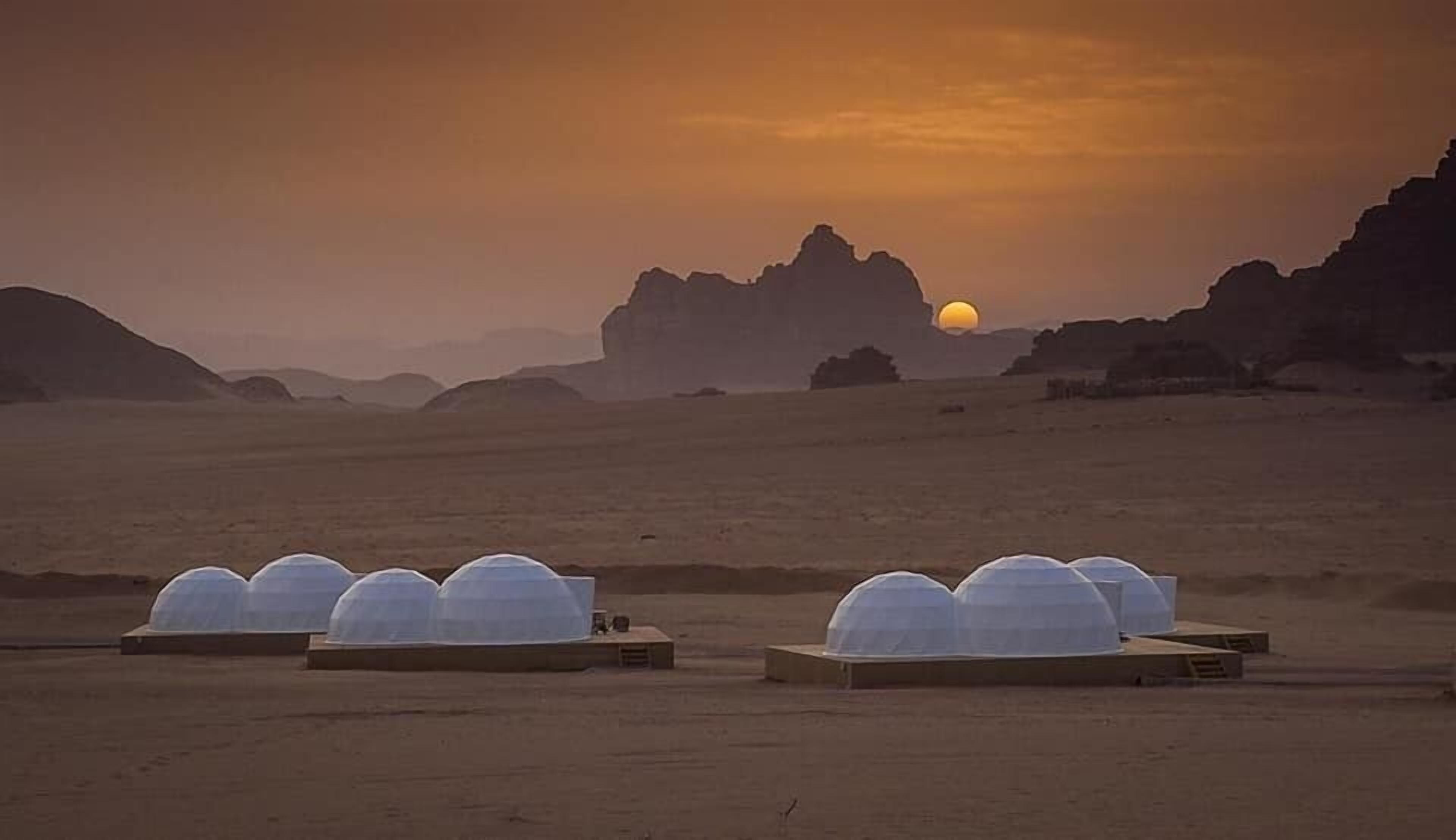 Paisaje desértico con varias estructuras en forma de cúpula, presumiblemente para observación o investigación, bajo un cielo al atardecer.