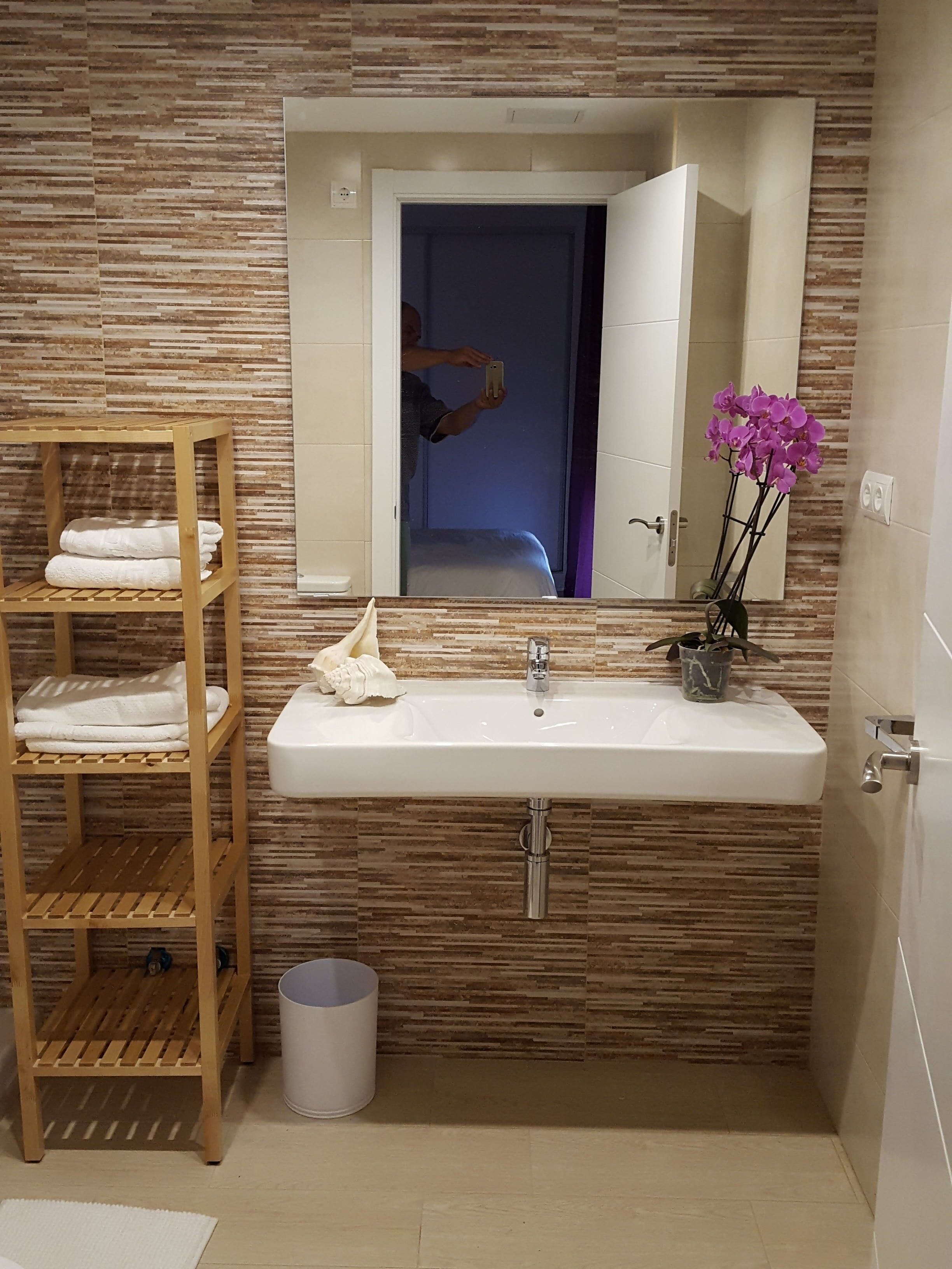Ein Badezimmer mit einem Holzboden, Handtüchern, einem Waschbecken mit Spiegel und einer Orchidee im Topf.