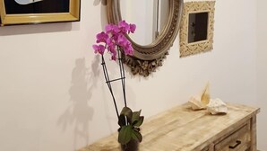 Ein Holzkonsolentisch mit zwei Schubladen, ein Spiegel mit aufwendiger Rahmung und ein kleiner dekorativer Topfpflanze mit violetten Blüten.