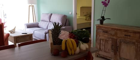 A dining area with a wooden table, red chairs, a fruit basket, a white sofa, and a wooden cabinet.