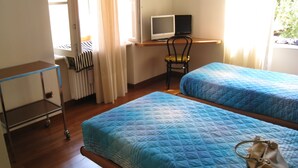 A room with two beds, a desk with a computer, a chair, a radiator, and a cart. - Elisabetta Rapallo's house (Rapallo)