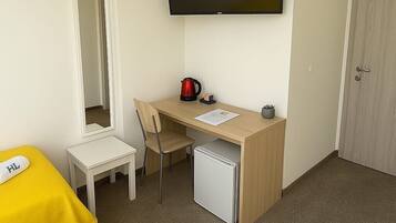 Habitación de hotel con cama, escritorio, silla, televisión, refrigerador pequeño y puerta.