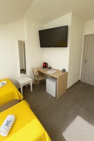 Habitación de hotel con cama, escritorio, silla, televisión, refrigerador pequeño y puerta.