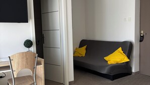 Hotellihuone, jossa on työpöytä, tuoli ja keltainen koristetyynyin varustettu sohva.