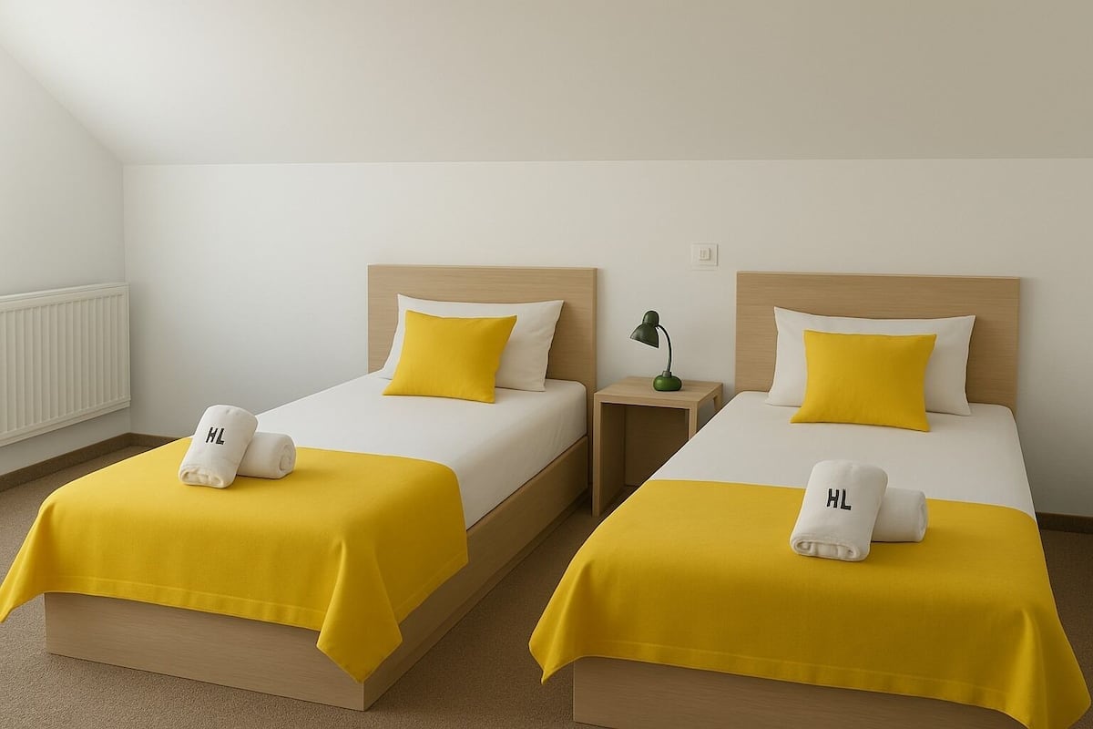Two single beds with yellow bedding and white pillows, each with a towel labeled 'HL'.
