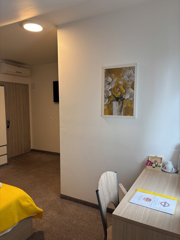 A hotel room with a dining area, a painting on the wall, and a small table with a tray.