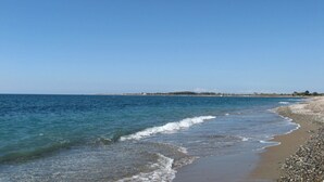 Ein Strand mit klarem, blauem Wasser, Kiesufer und einer entfernten Landmasse.