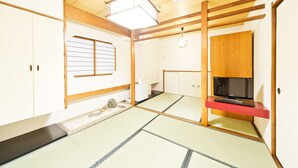 Una habitación japonesa tradicional con suelo de tatami, un televisor sobre un pedestal rojo y puertas correderas de madera.