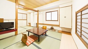 Una habitación japonesa tradicional con suelo de tatami, una mesa baja, televisor y puertas correderas.