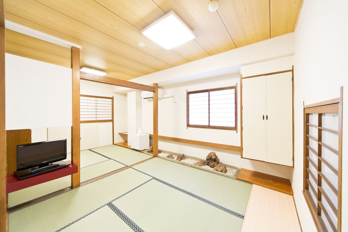 A traditional Japanese room with tatami flooring, a television on a low shelf, and sliding doors.