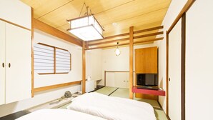 Una habitación de estilo japonés tradicional con suelo de tatami, un futón, un televisor y una puerta corredera.