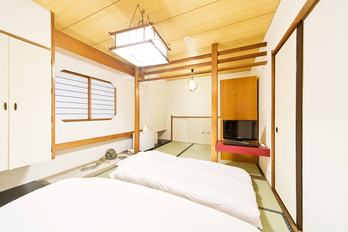 Une pièce de style japonais traditionnel, avec un sol recouvert de tatamis, un futon servant de lit, une télévision et une porte coulissante.