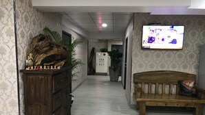 A hallway with patterned wallpaper, a wooden bench, a TV mounted on the wall, and a decorative wooden piece on a cabinet. - My House (Luodong)