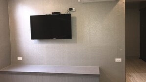 A room with a flat-screen TV mounted on the wall, a small table, and an air conditioning unit. - My House (Luodong)