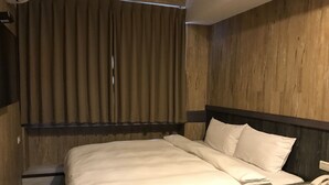 A hotel room with a wooden headboard, a bed with white linens, a bedside table with a phone, and a window with curtains. - My House (Luodong)