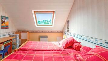 A bedroom with a skylight, a bed with red bedding, a desk with a chair, and a poster on the wall.