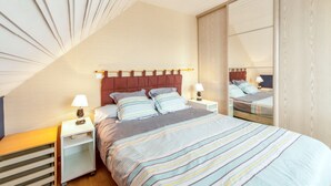 Een slaapkamer met een bed, nachtkastjes, een spiegel en een schuine plafond.