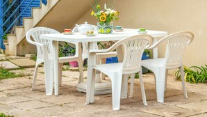 Een witte buitentafel met stoelen, een bloevas en een theepot.