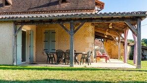 A covered outdoor patio with a table and chairs, a wooden pergola, and a view of a house with a tiled roof. - Homerez - Villa in Issac (Issac)