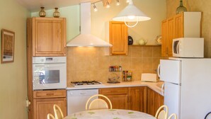 A kitchen with wooden cabinets, a stove, a microwave, and a dining table with chairs. - Homerez - Villa in Issac (Issac)