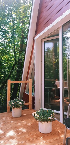 A wooden deck with two potted plants, a wooden ladder, and a sliding glass door leading to an outdoor area with a table and chairs. - Little break (Gossersweiler-Stein)