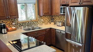 A modern kitchen with wooden cabinets, a stainless steel refrigerator, a built-in oven, and a granite countertop. - Mountain Retreat at Lake Cushman (Hoodsport)
