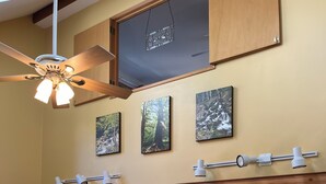 A spacious living room with a ceiling fan, a dining area with wooden chairs, a TV stand with a flat-screen TV, and a bookshelf. - Mountain Retreat at Lake Cushman (Hoodsport)