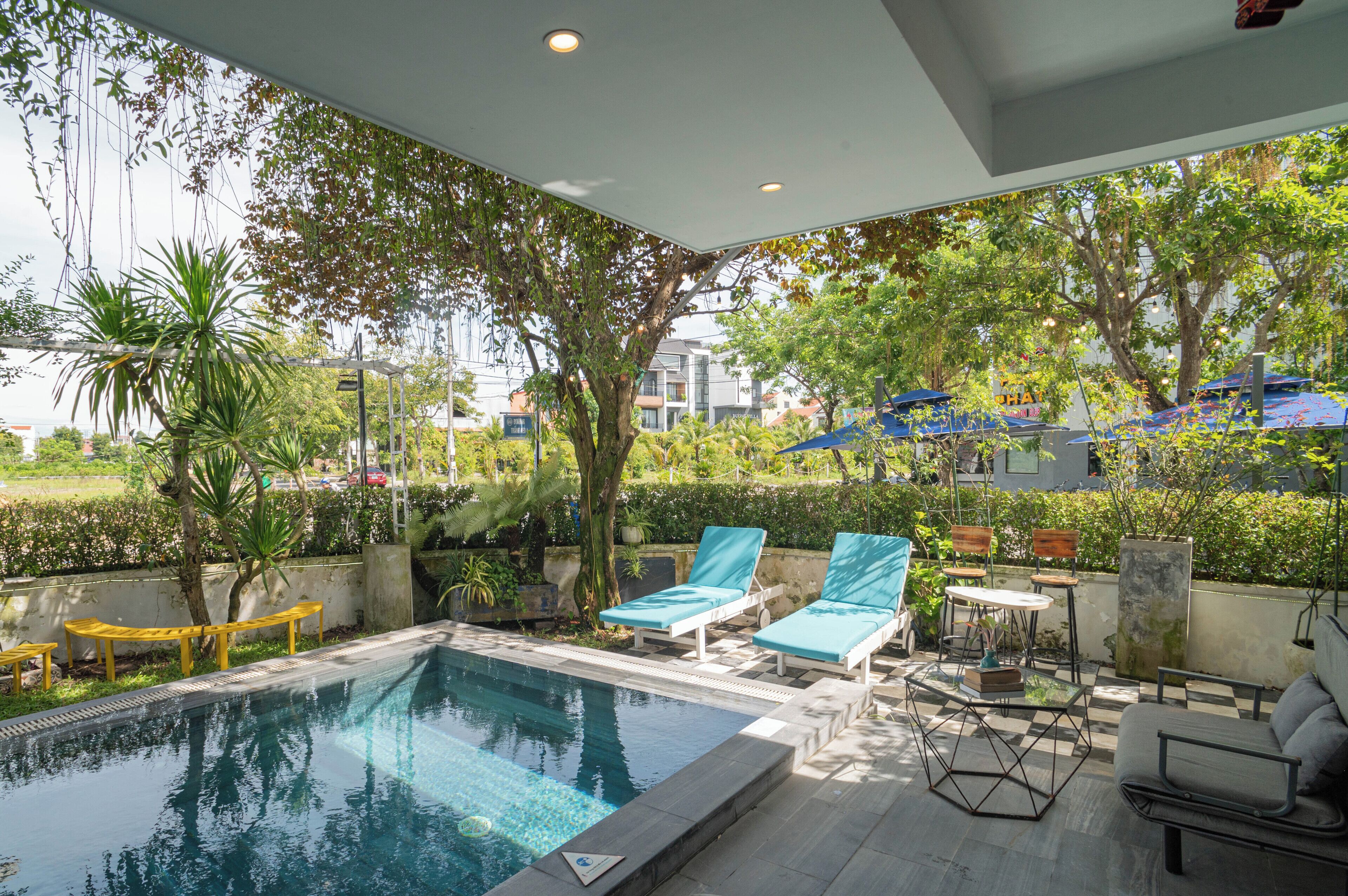 A pool area with lounge chairs and a table, surrounded by greenery and trees.
