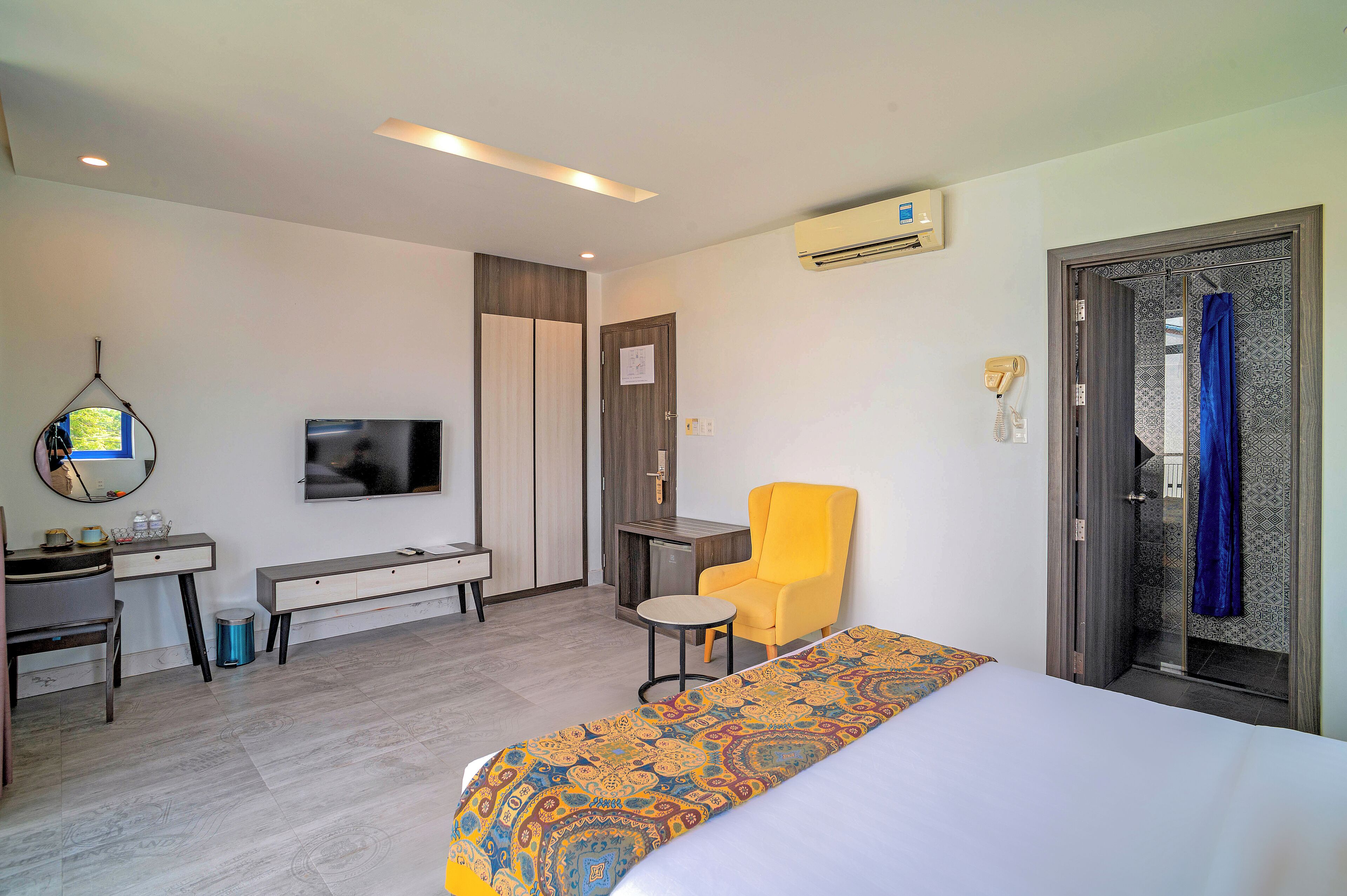 Quarto de hotel com cama, escrivaninha, cadeira, televisão e ar condicionado.