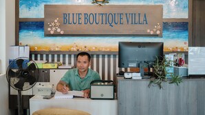 A reception desk with a sign reading "BLUE BOUTIQUE VILLA," a desktop computer, a fan, and a potted plant. - Blue Boutique Villa Hoi An (Da Nang)