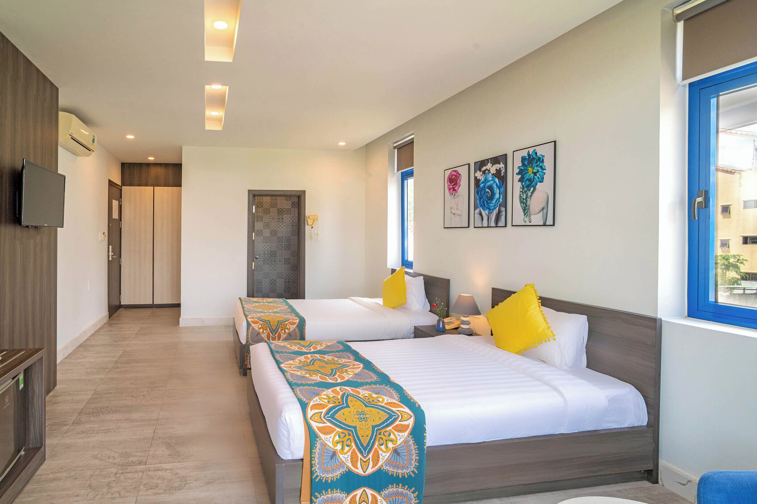 A hotel room with two beds, a TV, artwork on the wall, and a window.