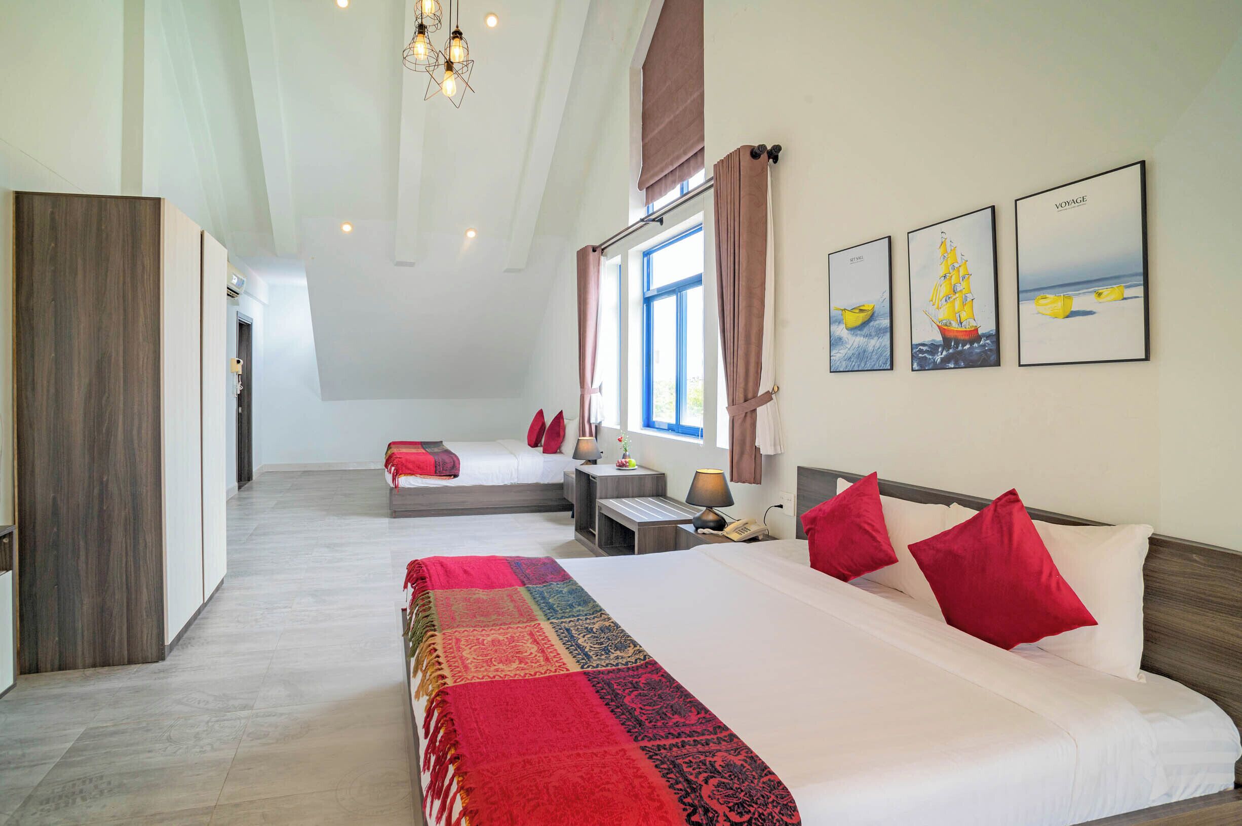 Una habitación de hotel con dos camas, un ventanal con cortinas, un candelabro y obras de arte en la pared.